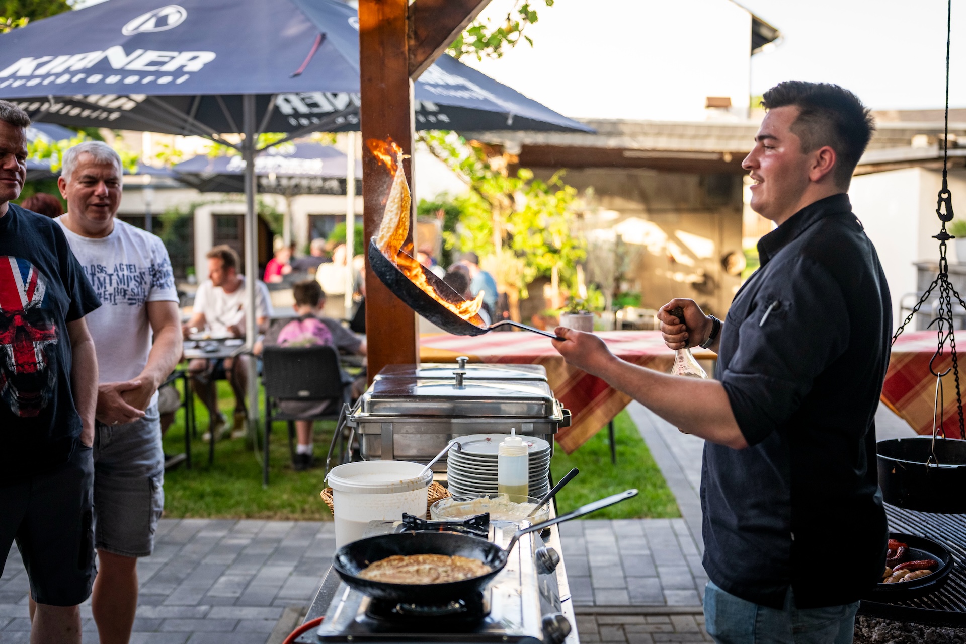 Moselhöhe - Koch flambiert Pfannkuchen vor zuschauenden Gästen im Biergarten des Landgasthauses Moselhöhe