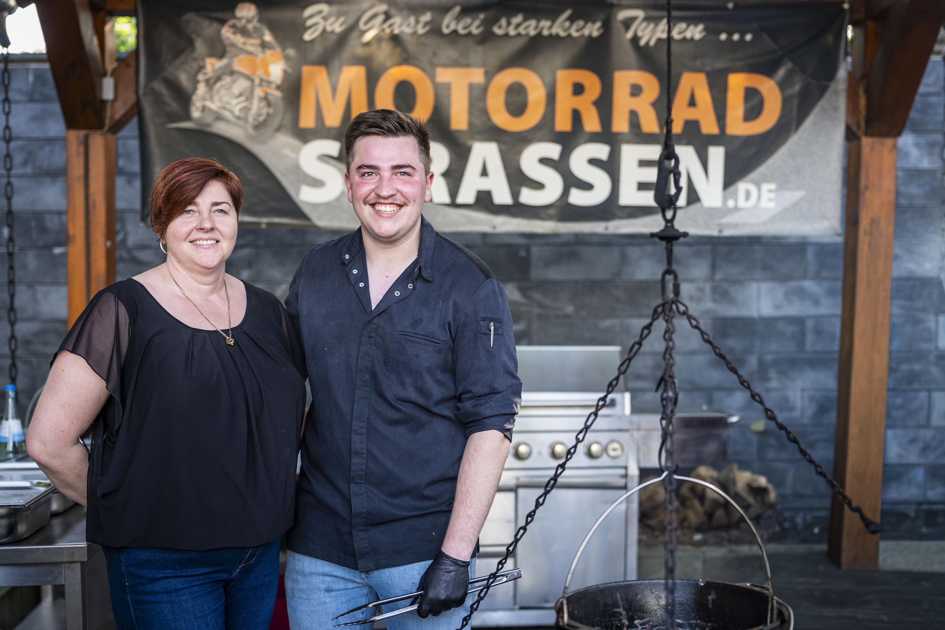 Moselhöhe - Gastgeber und Koch Paul Schmitz mit seiner Mutter vor der Außenküche und dem Schwenkgrill im Landgasthaus Moselhöhe